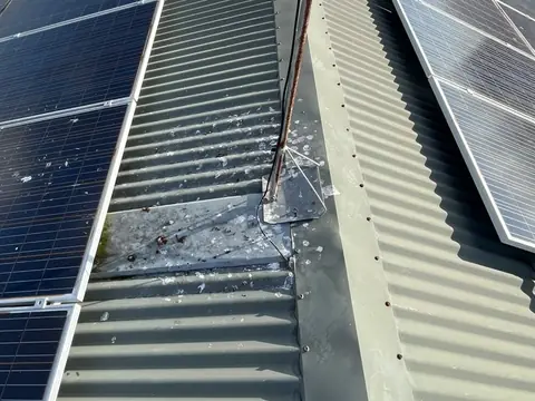 A TV antenna on a metal roof between two groups of solar panels, with bird droppings on the roof around it