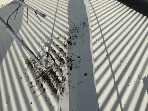 Bird droppings and debris on the ridge of a metal roof around the base of an old antenna