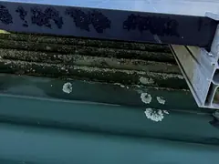 The open gap under the edge of a rooftop solar panel, with lichen on the metal roof below