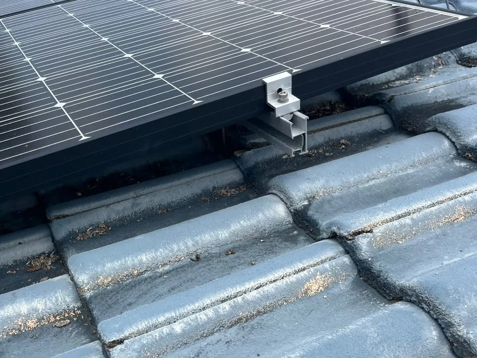 The edge of a solar panel on a tile roof, with debris in the gap underneath and husks scattered on the tiles in front