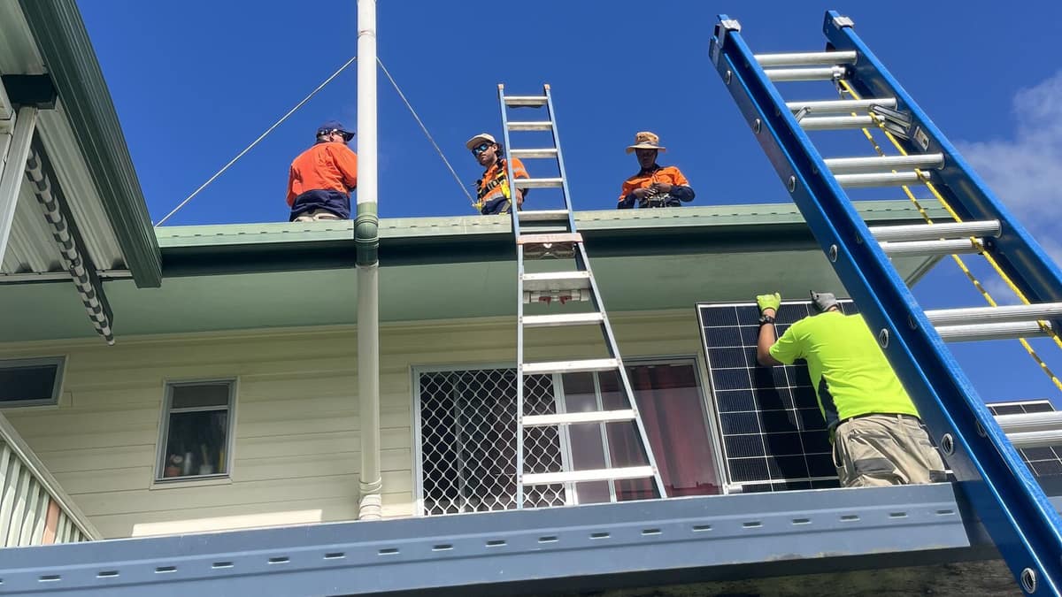 Crew lifting a solar panel up ladders to a two storey home in Mackay