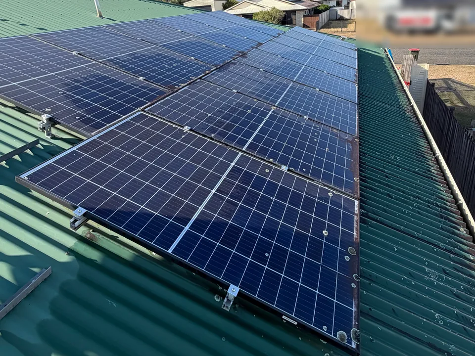 A solar array on a green metal roof in Mackay before cleaning, with a film of dust and lichen on the panels