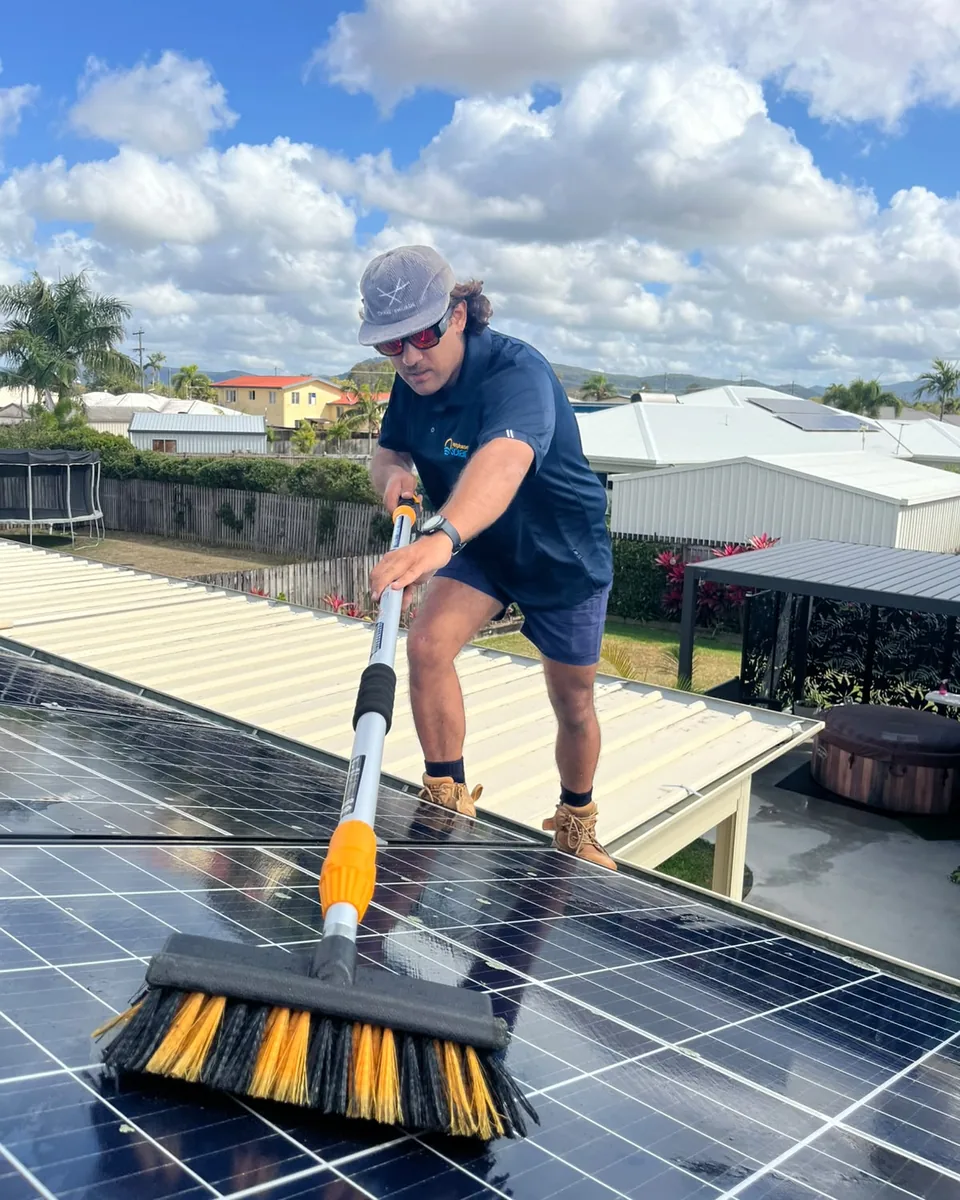 Next Phase Solar crew member scrubbing rooftop solar panels with a long brush on a sunny Mackay day