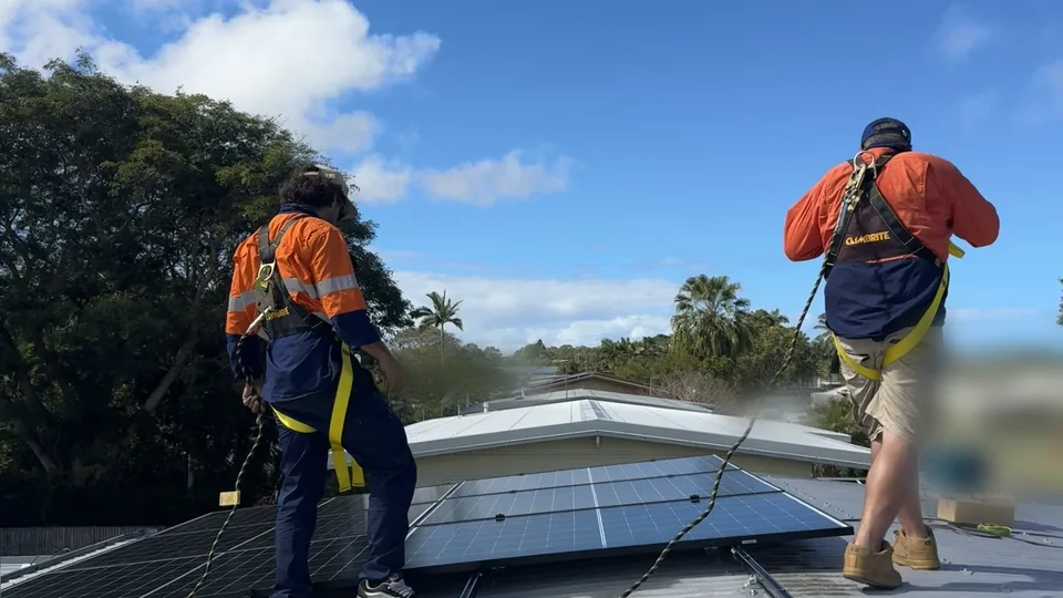 Two Next Phase Solar crew members in harnesses, from behind, on a metal roof in Mackay