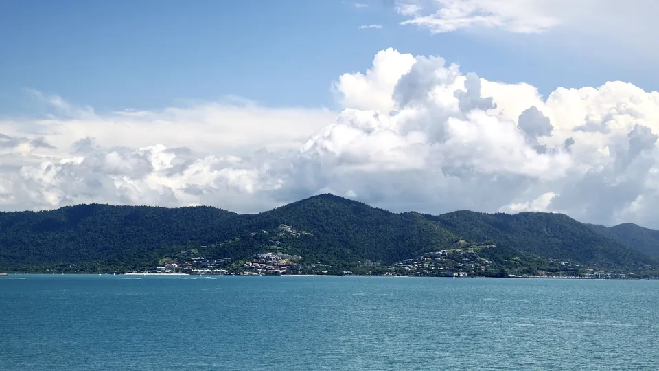 Airlie Beach and its green hills seen across the water under a cloudy sky