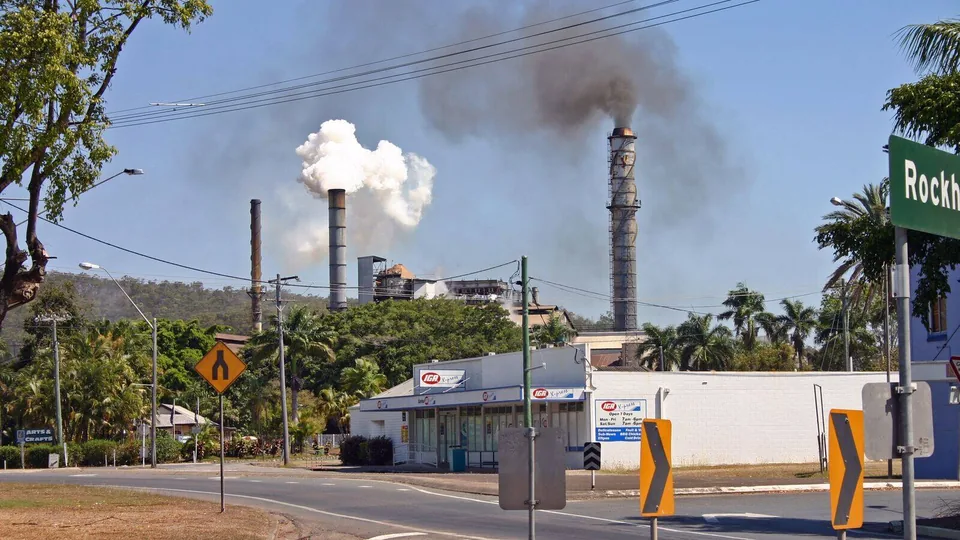 Sugar mill chimneys rising behind shops and a street corner in Sarina