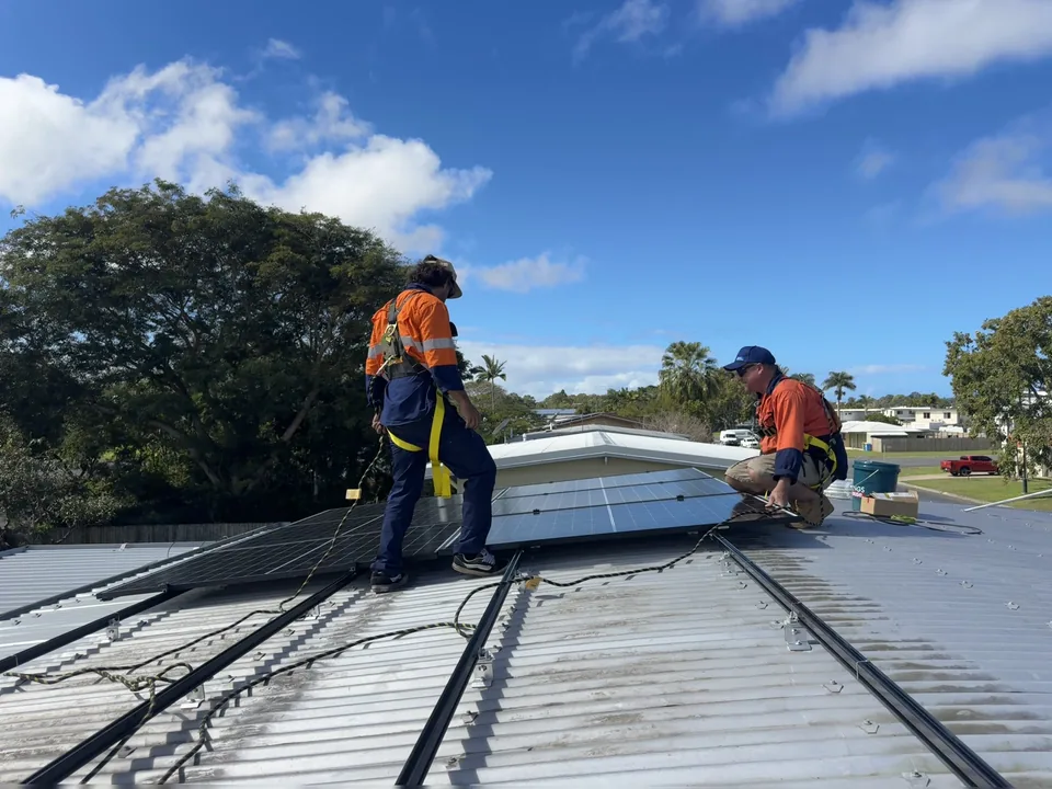 Two Next Phase Solar installers in harnesses fitting solar panels on a metal roof in Mackay