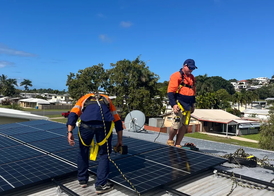 Two Next Phase Solar installers in harnesses laying solar panels on a metal roof
