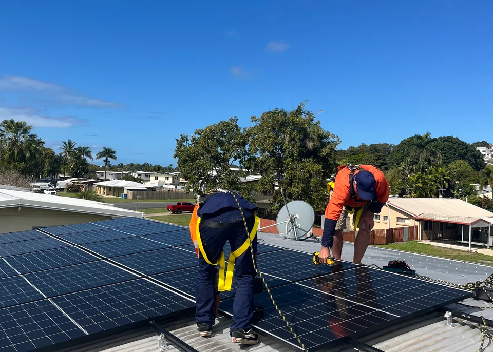 Two Next Phase Solar installers in harnesses fixing solar panels to rails on a metal roof